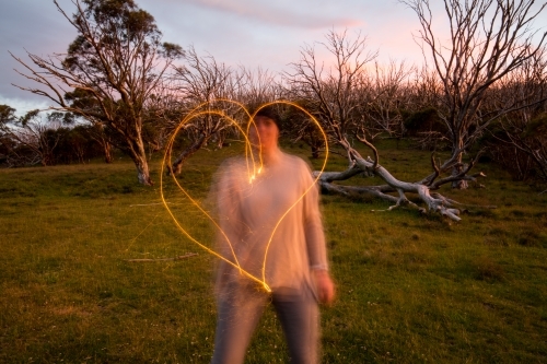 Woman making a heart shape with a sparkler at dusk