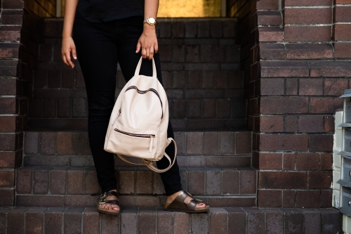 woman outside entrance to apartment building, with small stylish backpack - Australian Stock Image