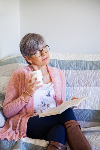 Woman reading a book on the lounge with cup of tea - Australian Stock Image