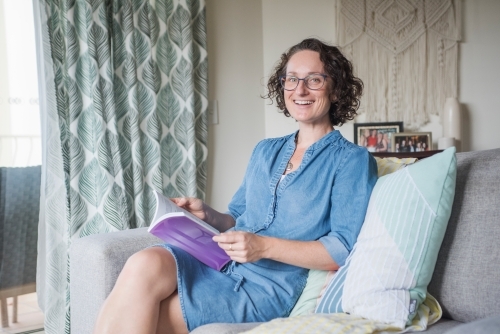 Woman reading book while seated on the couch - Australian Stock Image