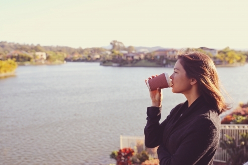 Woman relaxing and drinking coffee by the lake - Australian Stock Image