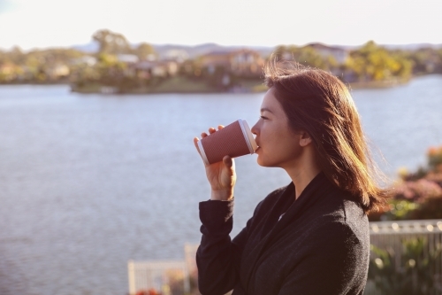 Woman relaxing and drinking coffee by the lake - Australian Stock Image