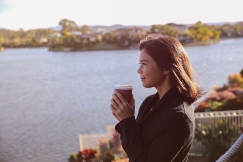Woman relaxing and holding cup of coffee by the lake - Australian Stock Image