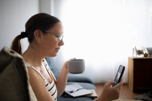 woman relaxing at home using smartphone and drinking coffee - Australian Stock Image