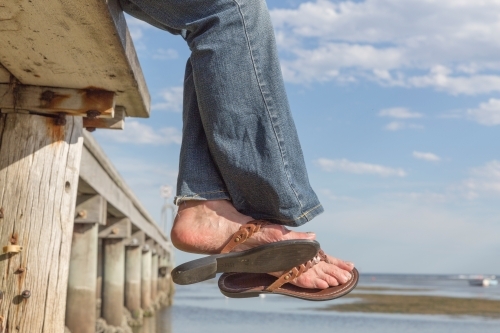 Woman's feet in sandals off the edge of a timber pier - Australian Stock Image