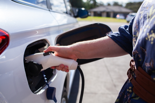 Woman’s hand plugging in hybrid car to charge EV battery in suburban driveway  - Australian Stock Image