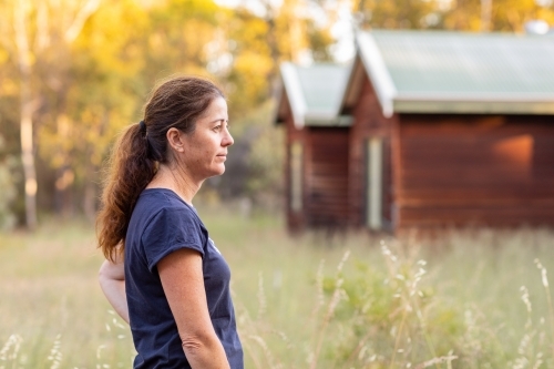 woman side-on outside timber cottage in the country - Australian Stock Image