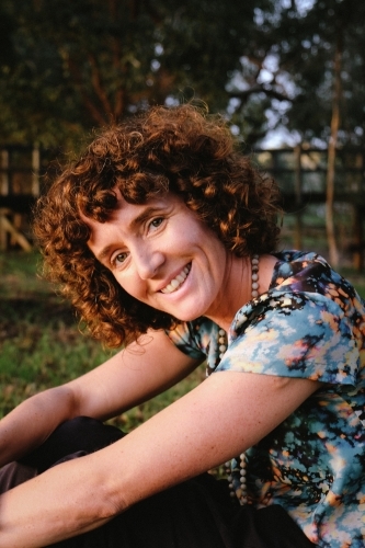 Woman sitting against trunk of tree in golden light - Australian Stock Image