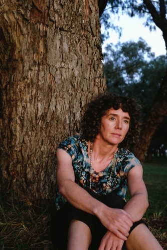 Woman sitting against trunk of tree in golden light - Australian Stock Image