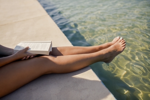Woman sitting at pool's edge holding book