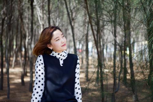 Woman sitting in front of a forest, happy and looking into the wind - Australian Stock Image