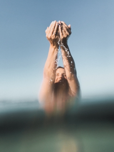 Woman sitting in glassy ocean and cupping water - Australian Stock Image
