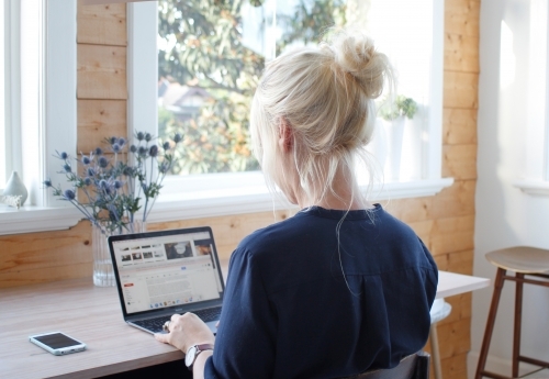 Woman sitting in sun room office working on laptop - Australian Stock Image