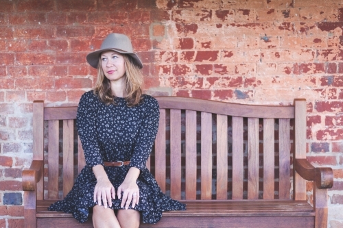 Woman sitting on a bench in front of a rustic wall - Australian Stock Image