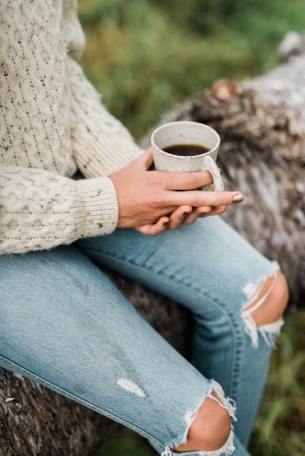 Woman sitting on a log holding a cup of coffee - Australian Stock Image