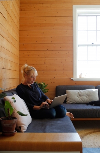 Woman sitting on couch working on laptop with timber wall background