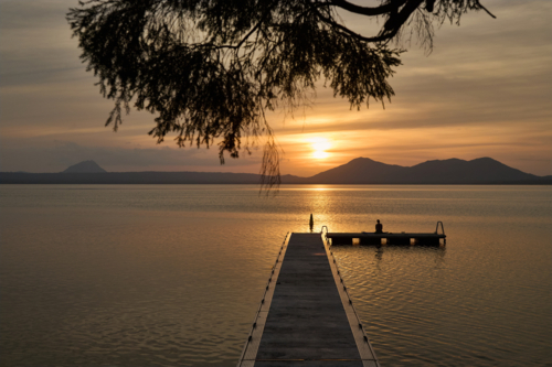 Woman sitting on jetty watching sunset - Australian Stock Image