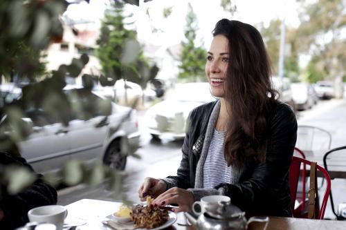 Woman sitting outdoors at cafe smiling and looking away - Australian Stock Image