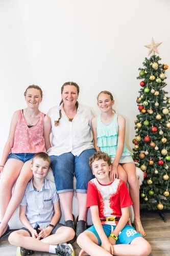 Woman sitting with four children with Christmas tree smiling - Australian Stock Image