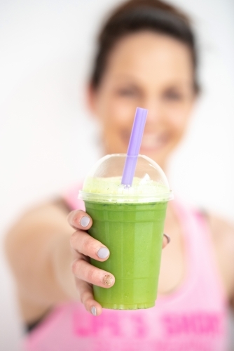 woman smiling holding green juice in workout clothes