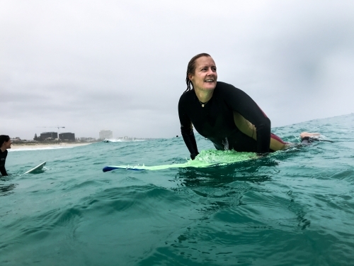 Woman smiling on surfboard in ocean on an overcast day