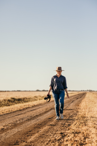 Woman smiling walking along a road carrying camera - Australian Stock Image