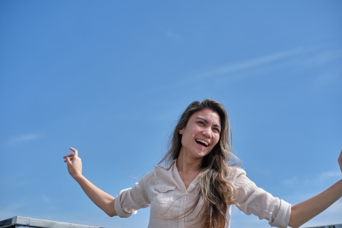 Woman smiling with arms out in front of blue sky - Australian Stock Image