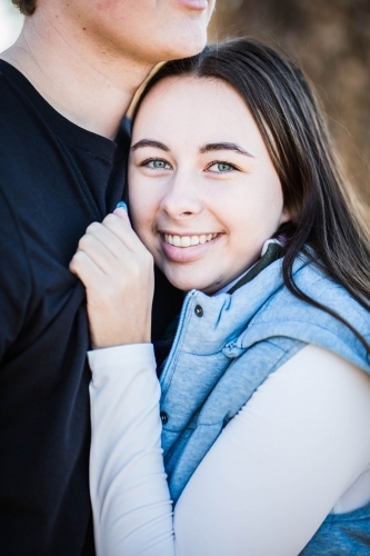 Woman snuggled in to boyfriend's chest smiling hand clutching shirt - Australian Stock Image