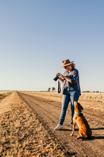 Woman standing in a dusty and dry grassy field holding a camera - Australian Stock Image