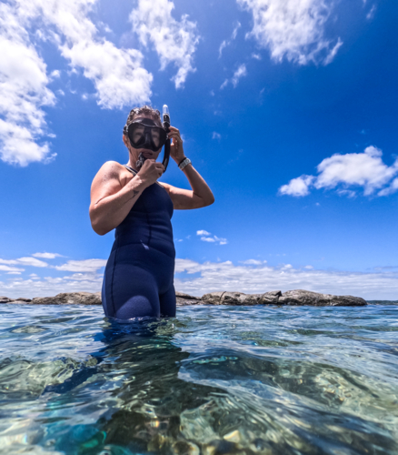 Woman standing in ocean in wetsuit adjusting snorkel ready to snorkel clear blue ocean water - Australian Stock Image