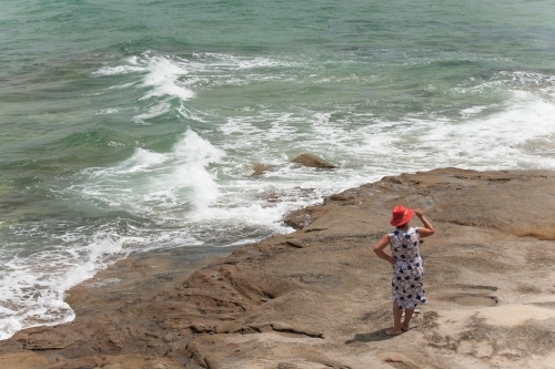 Woman standing on a rock looking out to the ocean - Australian Stock Image