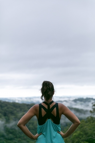 Woman standing on cliffs edge looking out at the rainforest view below - Australian Stock Image