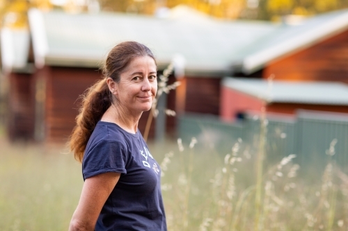 woman standing outdoors with wild oats and house in background - Australian Stock Image