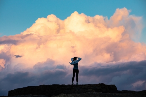 Woman standing with hands on head on rock against a dramatic cloud backdrop