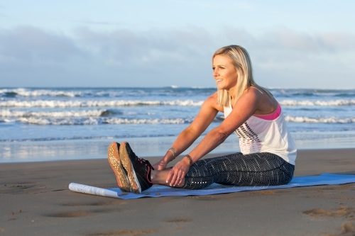 woman stretching on a mat at the beach - Australian Stock Image