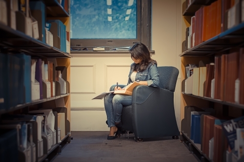 Woman studying on a chair in a library near book shelves