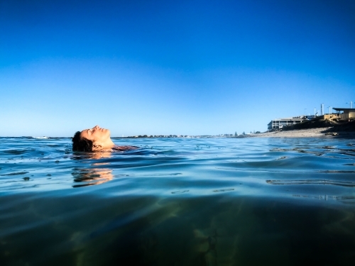 Woman submerged and floating in calm ocean on clear day - Australian Stock Image