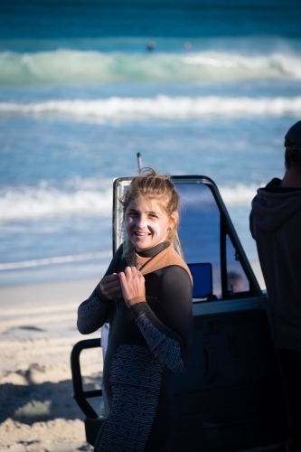 Woman suiting up for a surf next to 4WD on beach