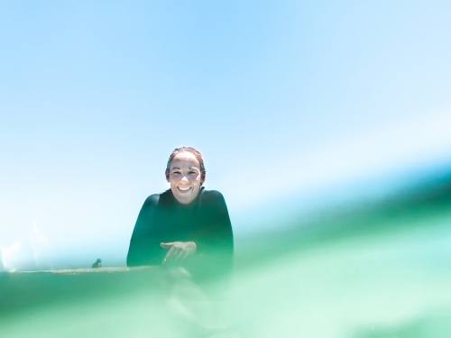 Woman surfer leaning on surfboard smiling at camera at sea level - Australian Stock Image