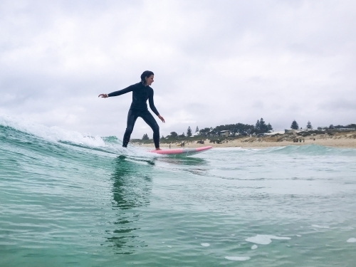 Woman surfing wave on soft board on overcast day - Australian Stock Image
