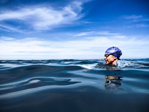 Woman swimming breastroke in cap and goggles in glassy ocean