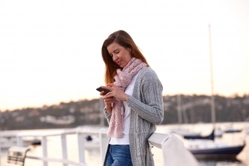 Woman using mobile phone on wharf during winter - Australian Stock Image