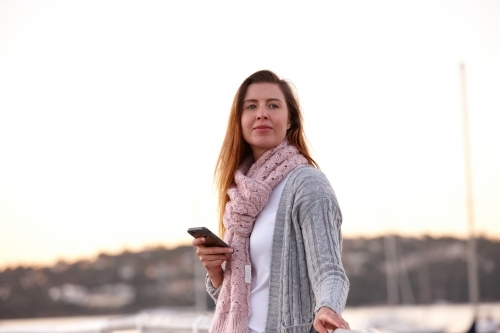 Woman using mobile phone on wharf wearing scarf - Australian Stock Image
