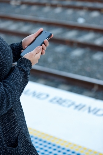 Woman waiting at train station holding mobile phone - Australian Stock Image