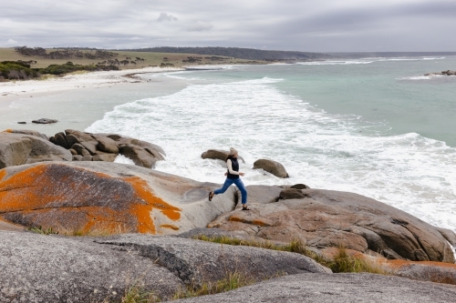 Woman walking across rocks by the ocean