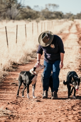 Woman walking dogs on red dirt track.