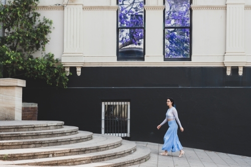 woman walking in the city, jacaranda season - Australian Stock Image