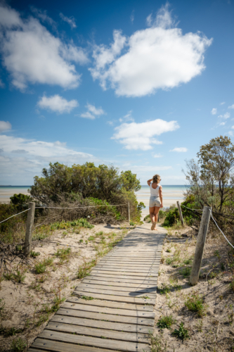 woman walking on slat wood beach path with beach in background - Australian Stock Image