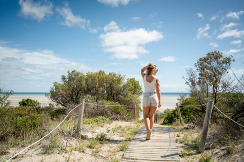 woman walking on slat wood beach path with beach in background - Australian Stock Image