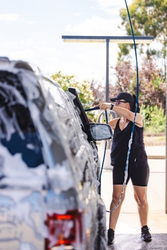 Woman washing vehicle in self-service car wash bay - Australian Stock Image